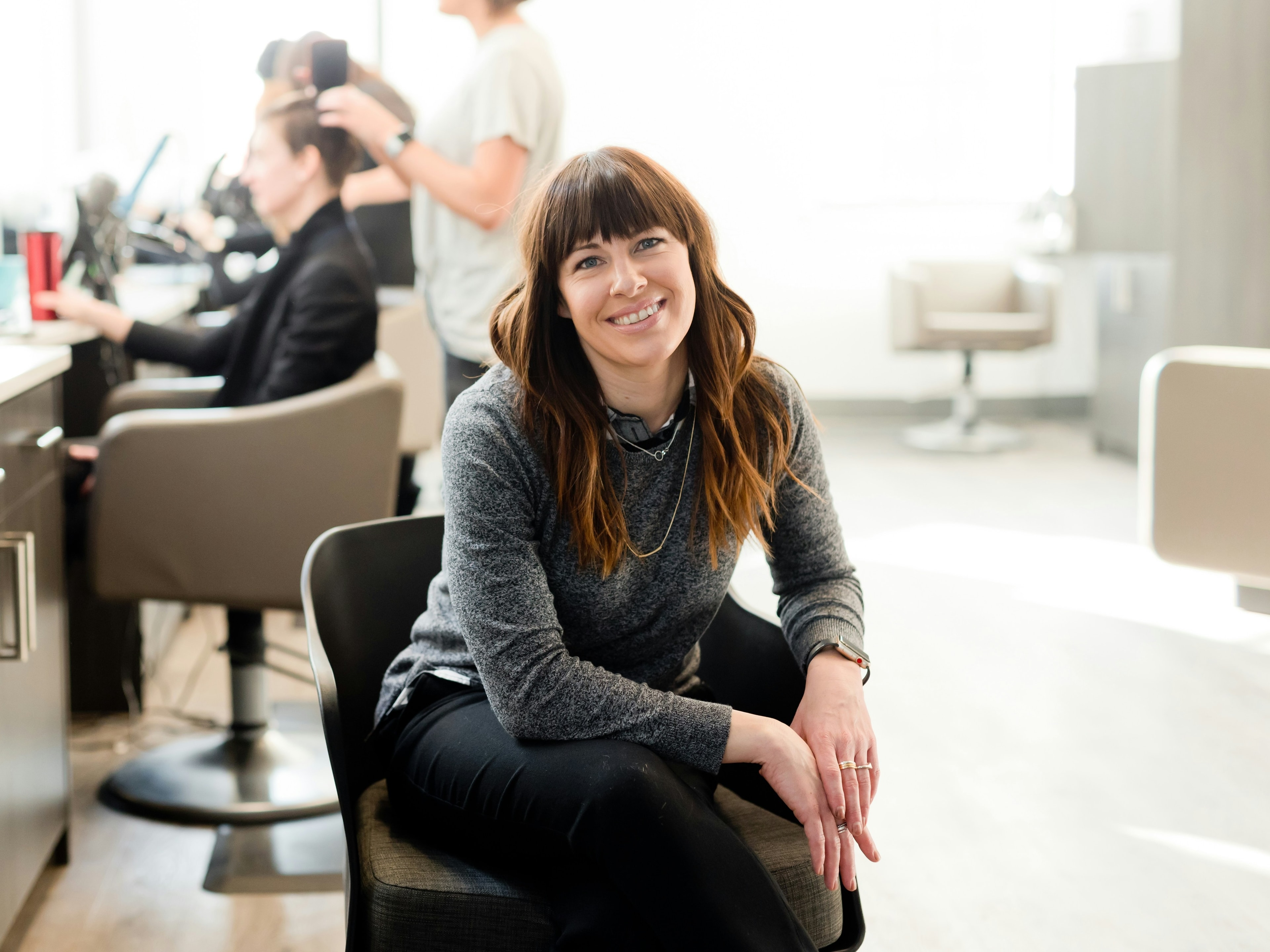 A woman seated in a salon while a hairdresser works with a client